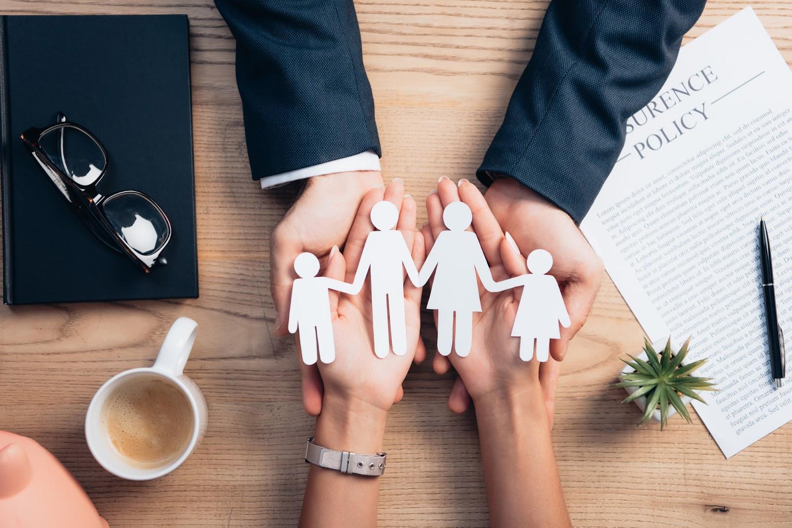 A male family lawyer holds his hands beneath a female client’s as she holds a paper family, symbolizing the support these attorneys can provide their clients when dealing with family conflict.