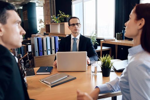 Divorcing spouses face each other during discussion in a mediator’s office while mediator takes notes on a laptop computer; concept for benefits of divorce mediation.